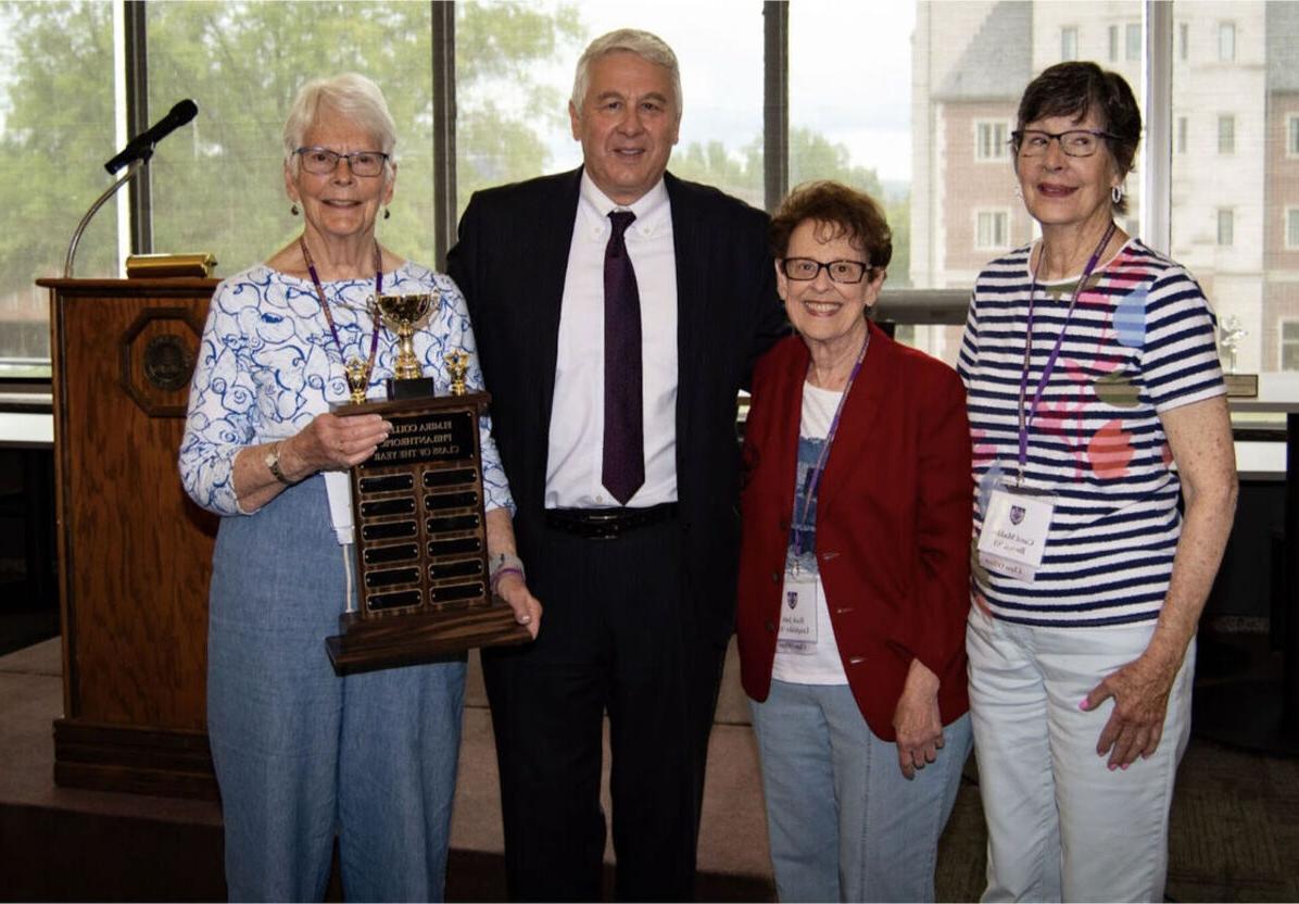 在2023年的聚会上，1963届的三名女学生与林赛校长站在一起，拿着年度慈善奖